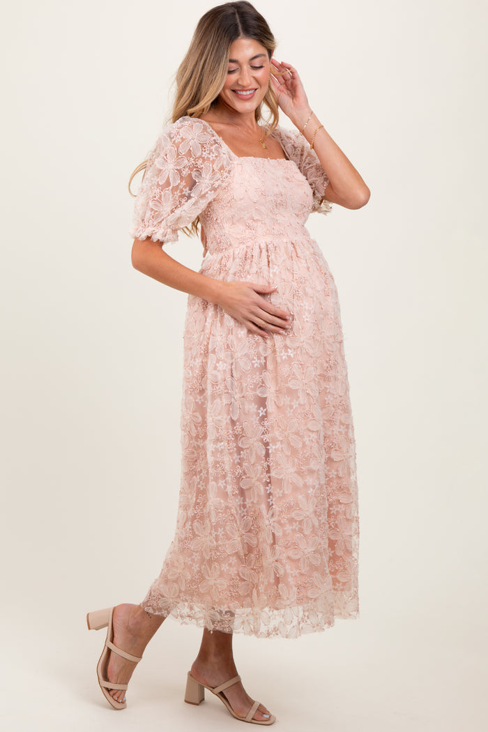woman wearing a blush pink lace maternity dress with short puff sleeves and holding her baby bump