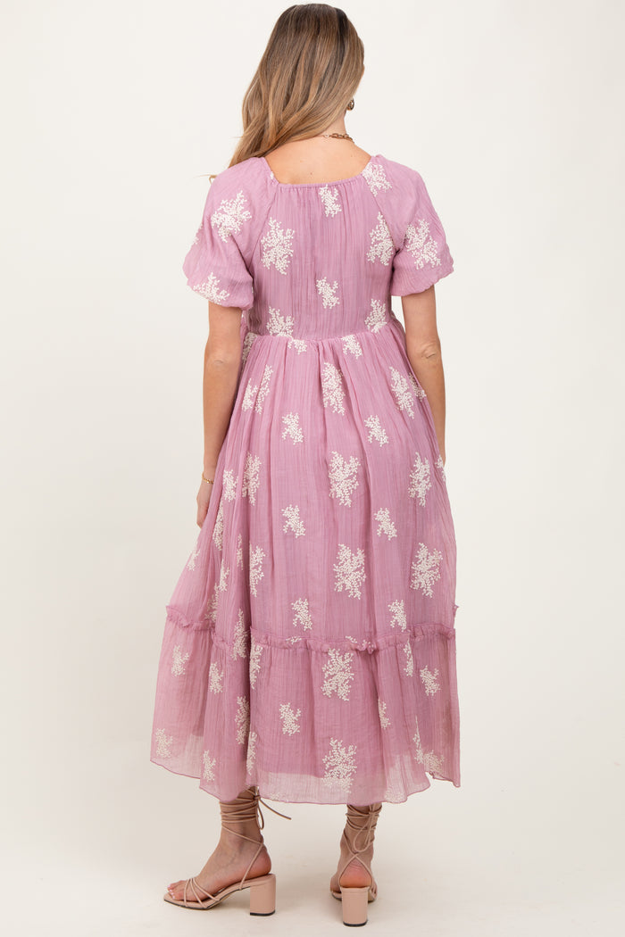 woman wearing a lilac maternity dress with white floral embroidery and a tiered hem, seen from the back