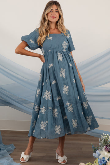 woman wearing a blue maternity dress with short puff sleeves and floral embroidery, showcasing a baby bump