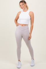 woman wearing a white cropped tank top and light gray high-waisted leggings, posing with a smile