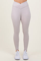 woman wearing light grey high-waisted leggings with a crisscross waistband and white athletic shoes
