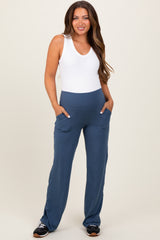 woman wearing a white tank top and blue maternity pants with pockets, standing and smiling
