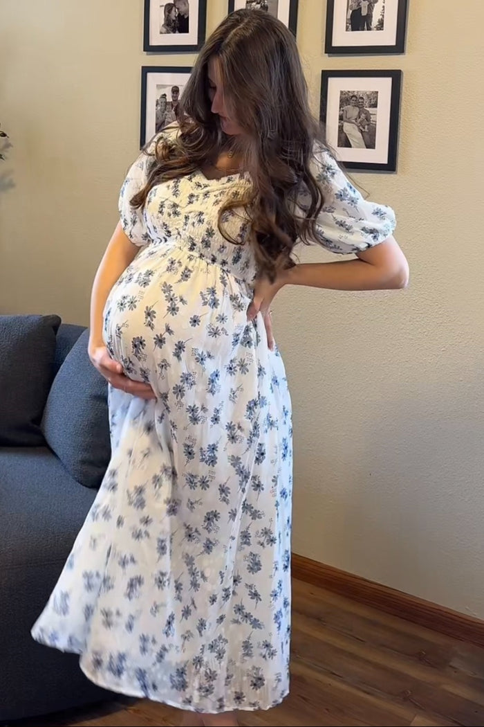 woman wearing a flowy white floral maternity dress and gently holding her baby bump