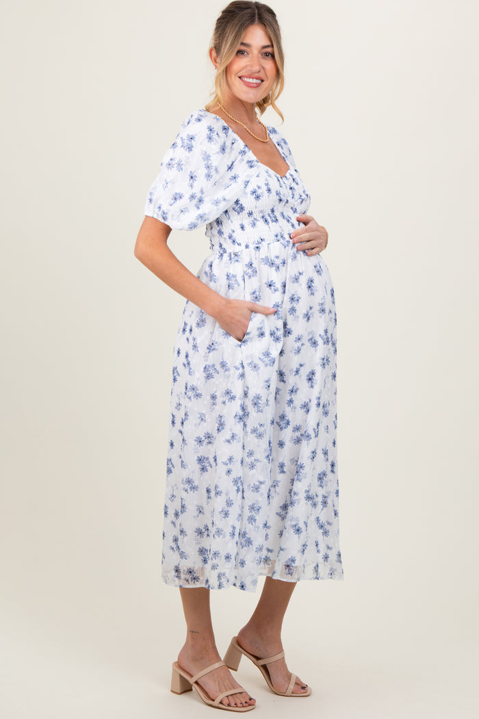 woman wearing a white floral maternity dress with puff sleeves, cinched waist, and pockets, showing her baby bump