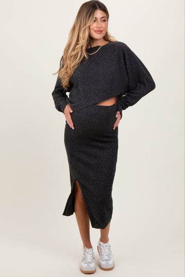 woman wearing a dark gray maternity crop top and matching skirt with a side slit, holding her baby bump
