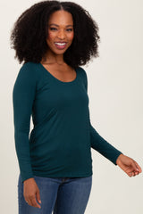 woman wearing a teal long sleeve top and blue jeans, smiling and posing to the side