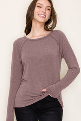 woman wearing a mauve long sleeve top with a relaxed fit and side pockets, smiling against a neutral background