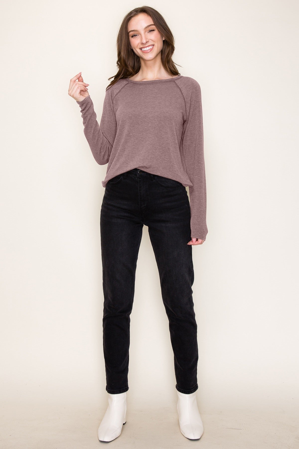 woman wearing a mauve long sleeve top and black skinny jeans, standing and smiling