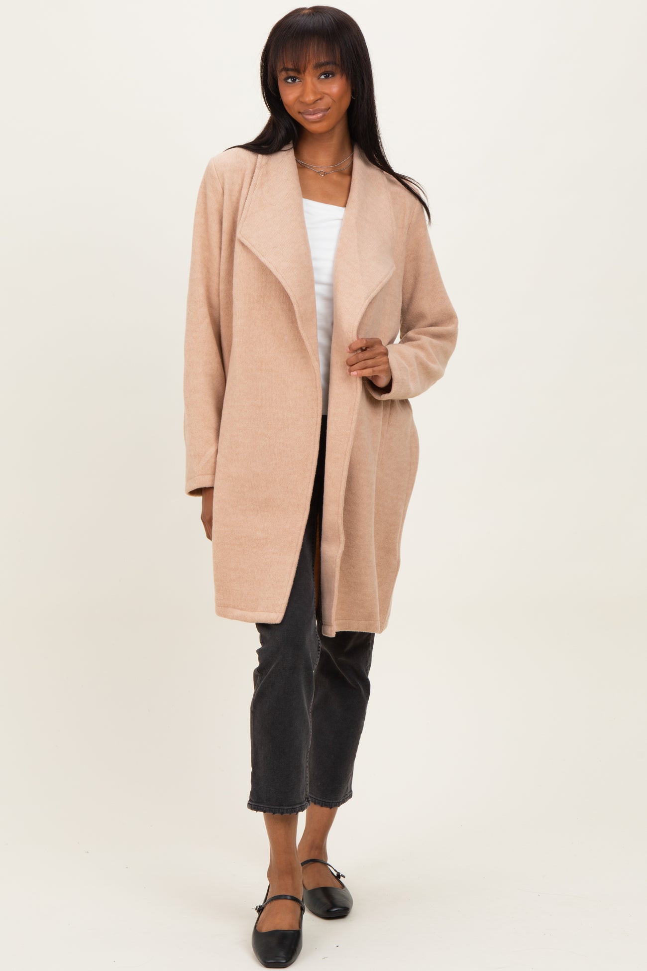 woman wearing a light beige open front cardigan over a white tank top and black jeans