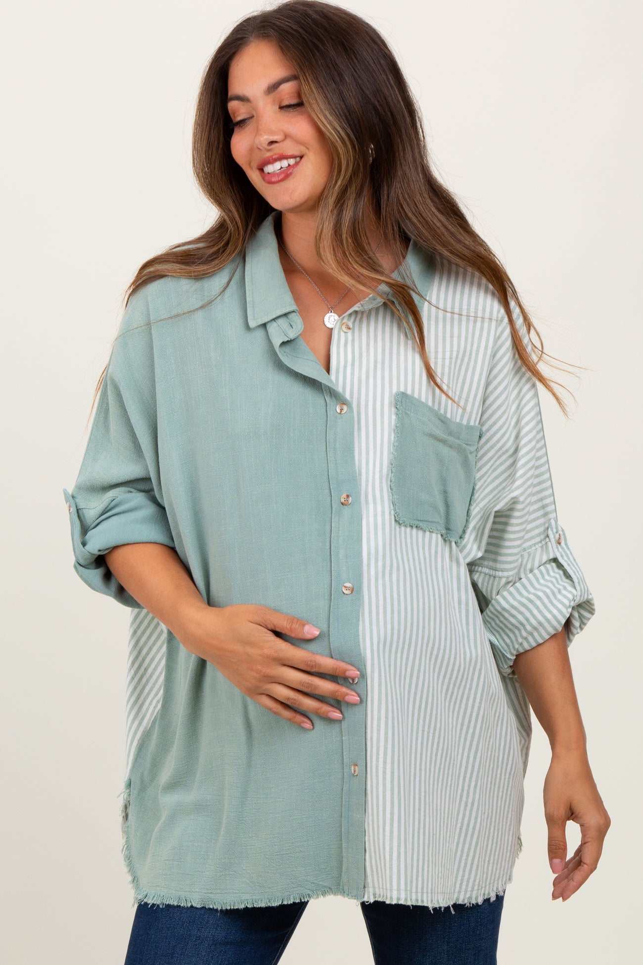 woman wearing a green and striped button-up maternity shirt, smiling and holding her baby bump