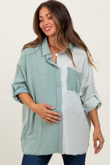 woman wearing a green and striped button-up maternity shirt, smiling and holding her baby bump