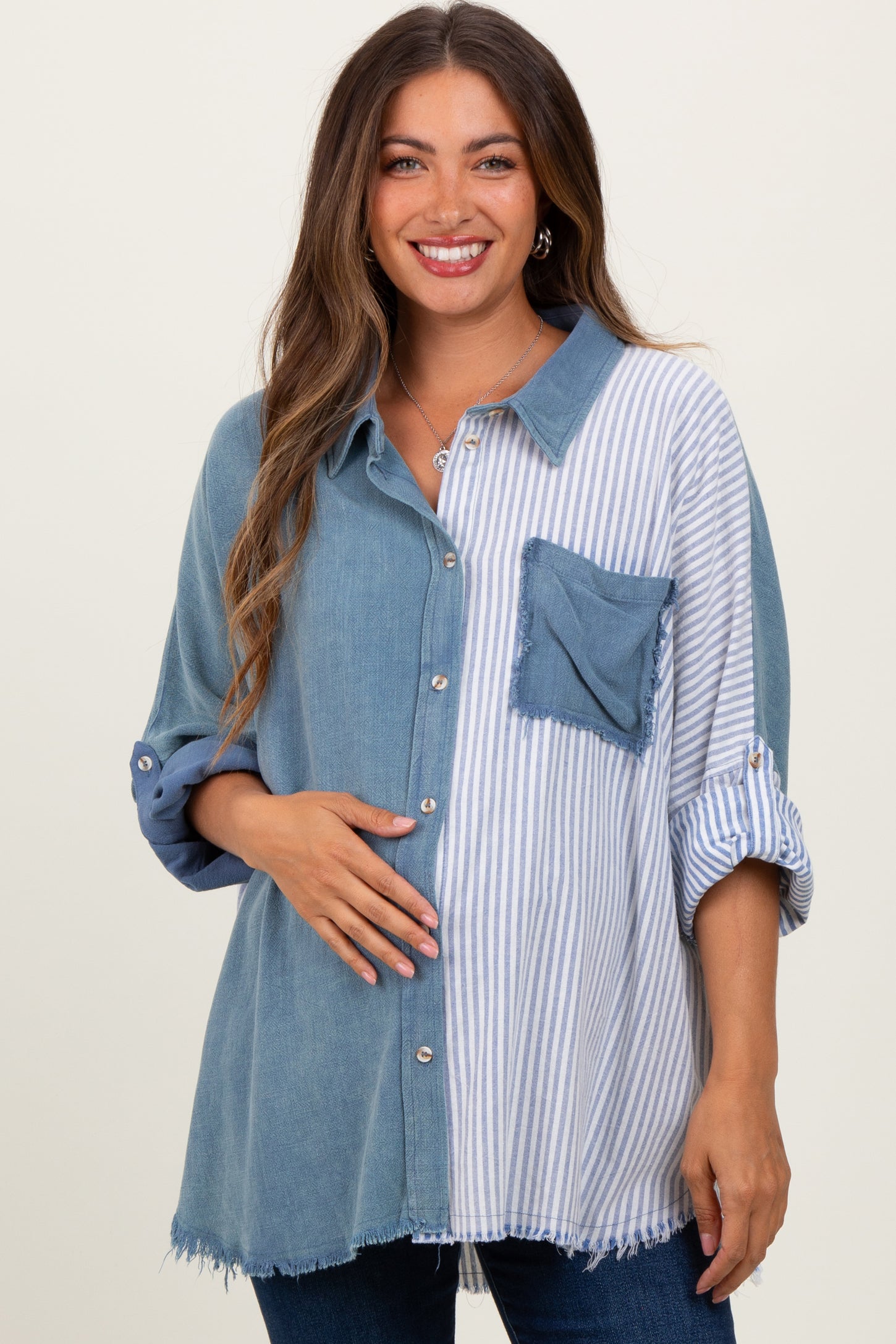 woman wearing a maternity oversized button-up shirt with denim and striped patterns, holding her baby bump