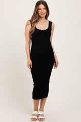 woman wearing a black ribbed maternity dress with scalloped edges and a fitted silhouette, showing a baby bump