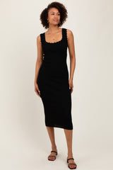 woman wearing a black ribbed midi dress with scalloped neckline and straps, standing against a light background