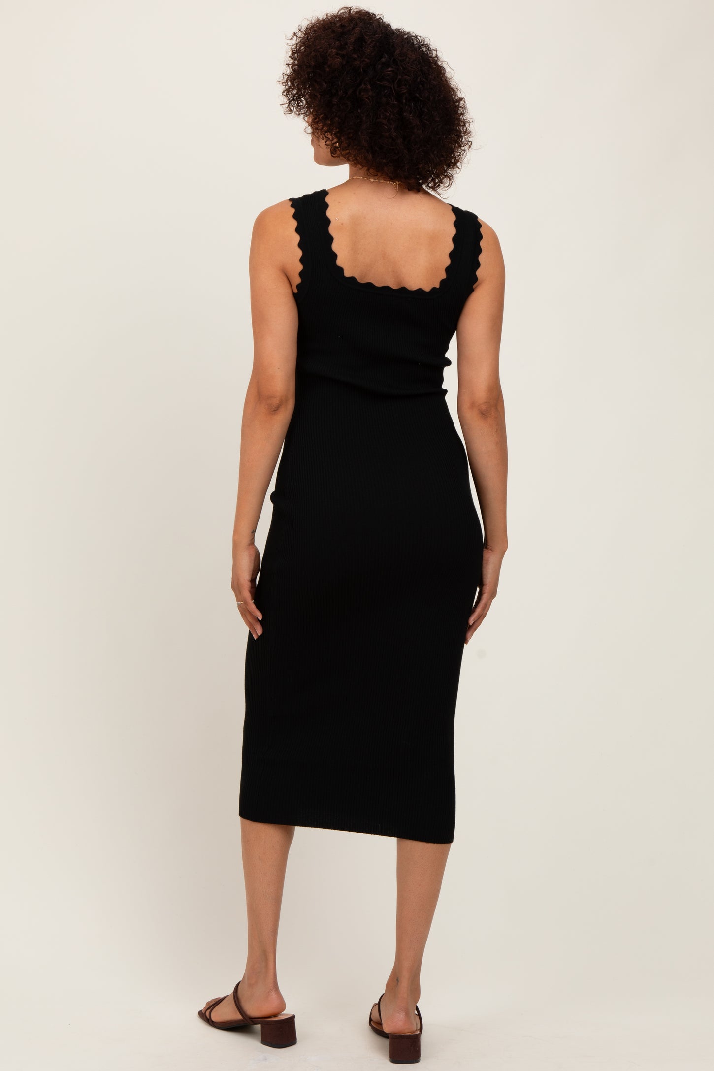 woman wearing a black ribbed midi dress with scalloped neckline and back, facing away from the camera