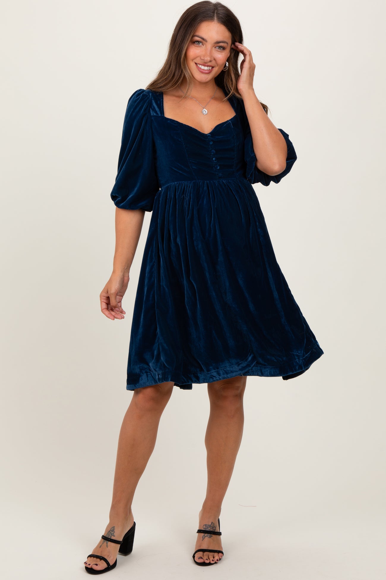 woman wearing a navy blue velvet maternity dress with puff sleeves and a square neckline