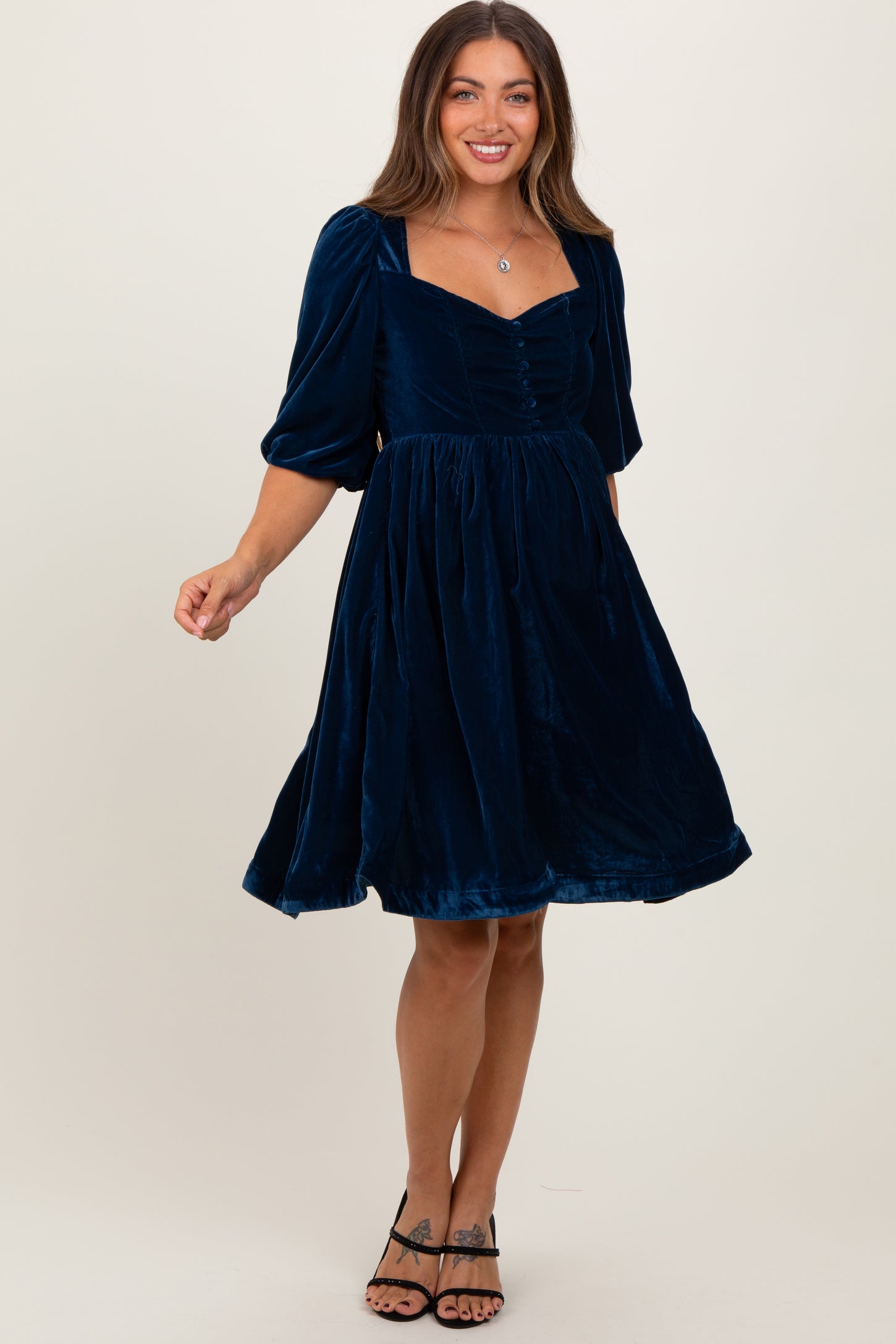 woman wearing a deep blue velvet maternity dress with puff sleeves and a square neckline, twirling playfully