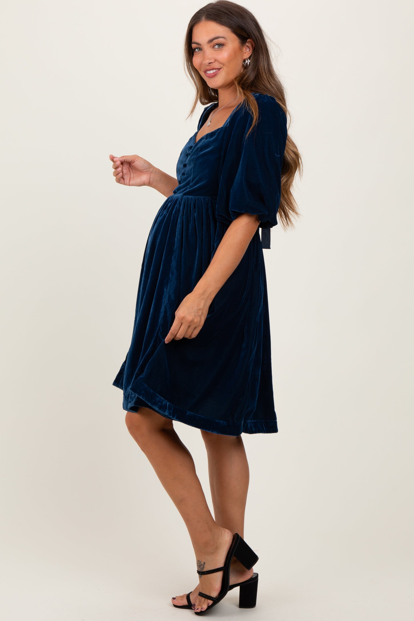 woman wearing a navy blue velvet maternity dress with a fitted bodice and puff sleeves, showing her baby bump