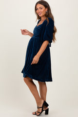 woman wearing a navy blue velvet maternity dress with a fitted bodice and puff sleeves, showing her baby bump