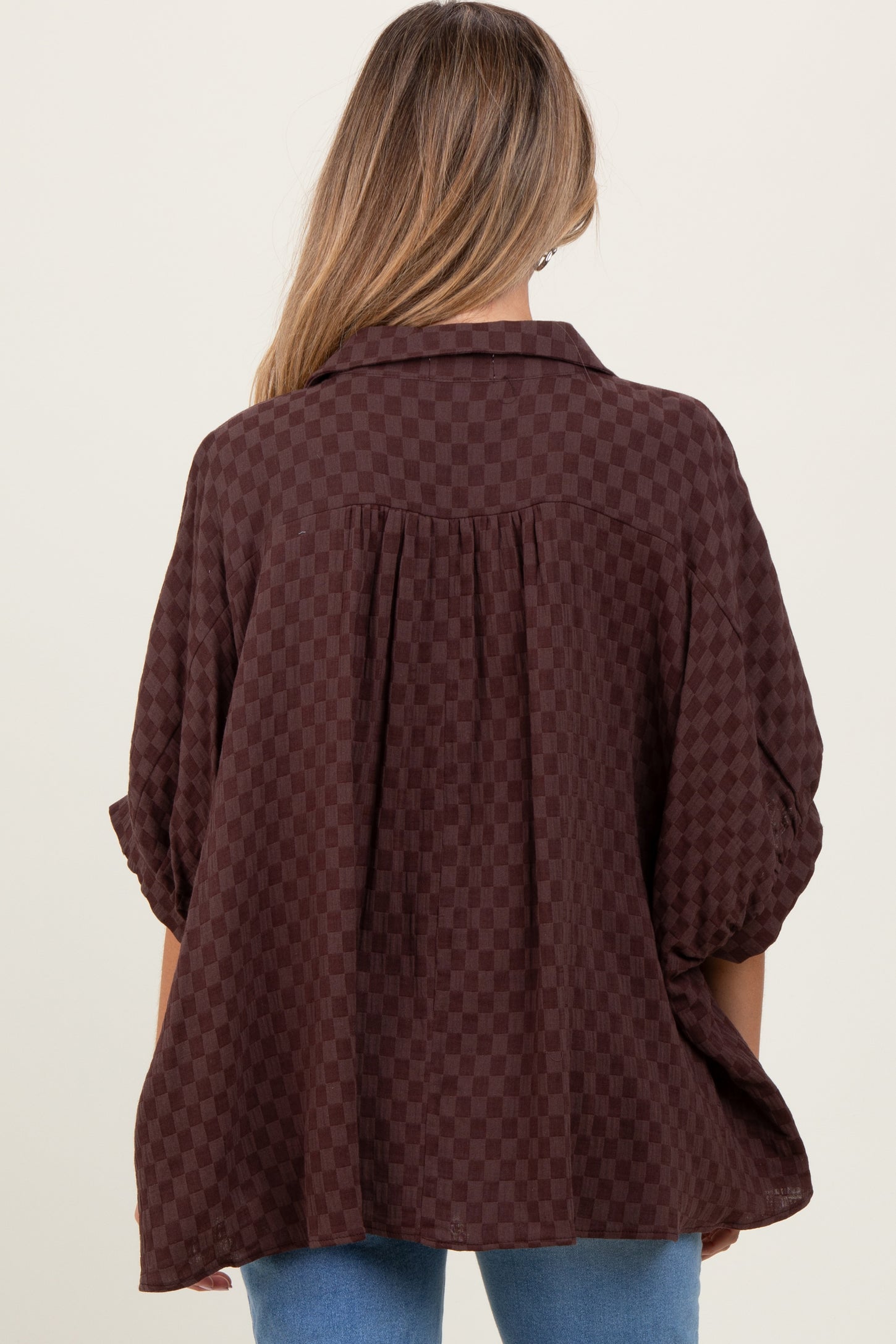 woman wearing a chocolate brown checkered maternity top with a relaxed fit and slightly puffed sleeves