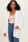 woman wearing an open front white knit cardigan over a beige tank top and high-waisted jeans