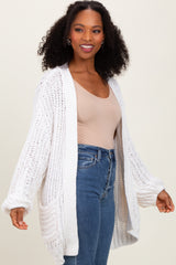 woman wearing a light beige fitted top and an oversized white knitted cardigan over high-waisted blue jeans
