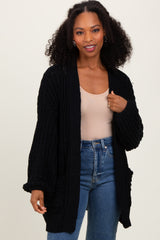 woman wearing a black knitted cardigan over a beige top and blue high-waisted jeans