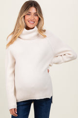 woman wearing a cream-colored maternity turtleneck sweater with a visible baby bump