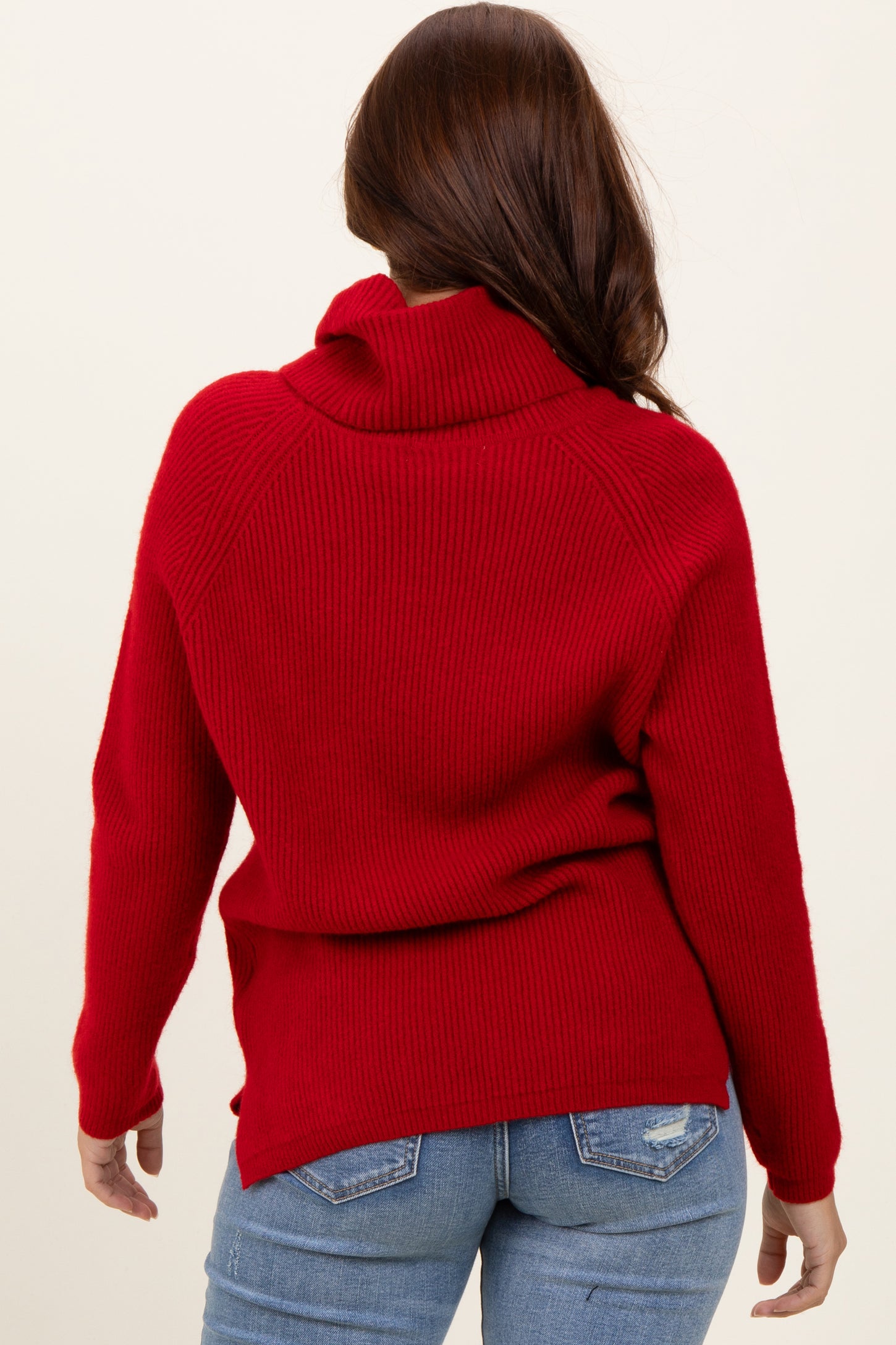 woman wearing a red ribbed cowl neck sweater paired with blue jeans, viewed from the back