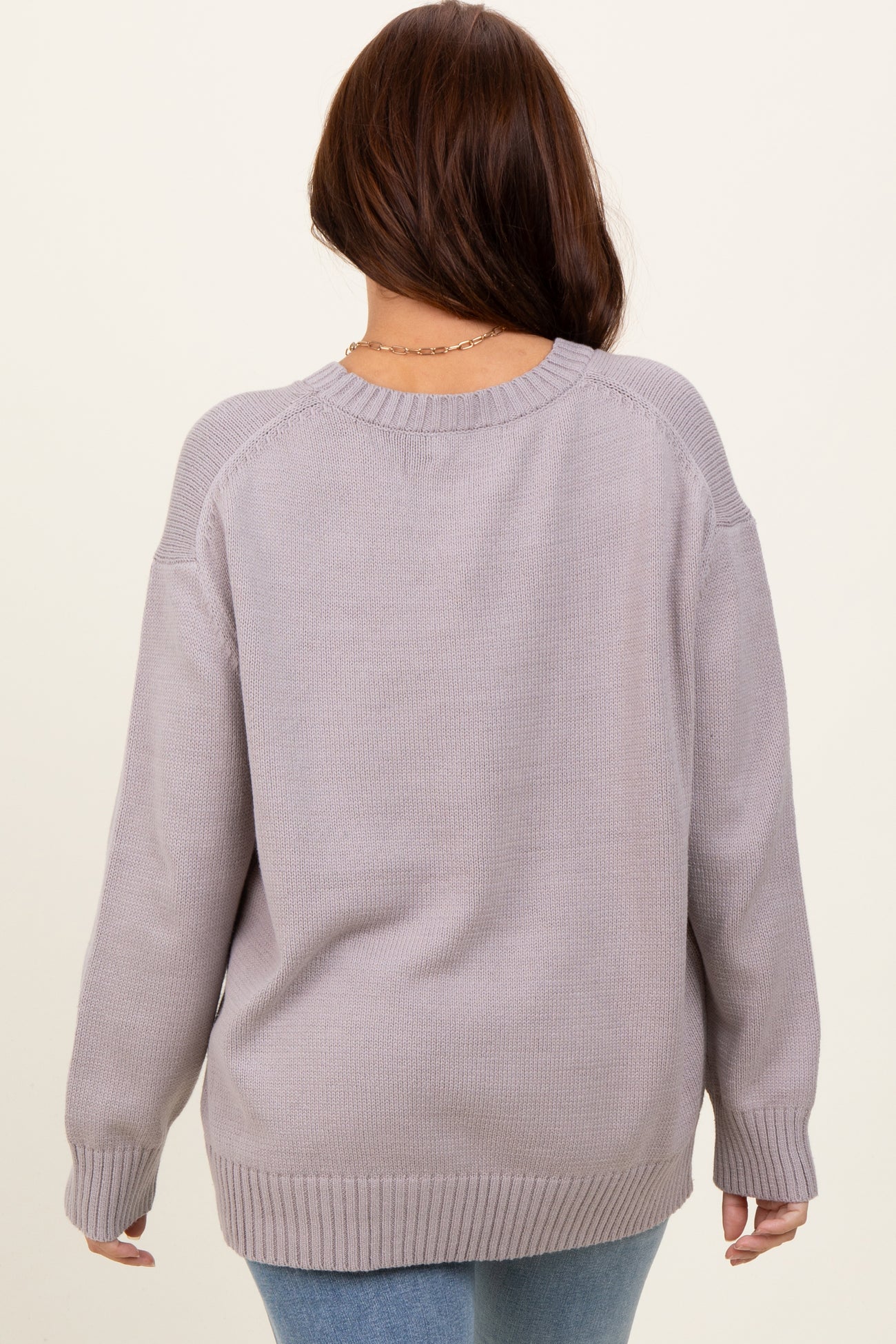 woman wearing a light gray oversized sweater with a round neckline and ribbed cuffs, viewed from the back