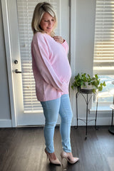 woman wearing a light pink oversized maternity sweater and blue skinny jeans, holding her baby bump