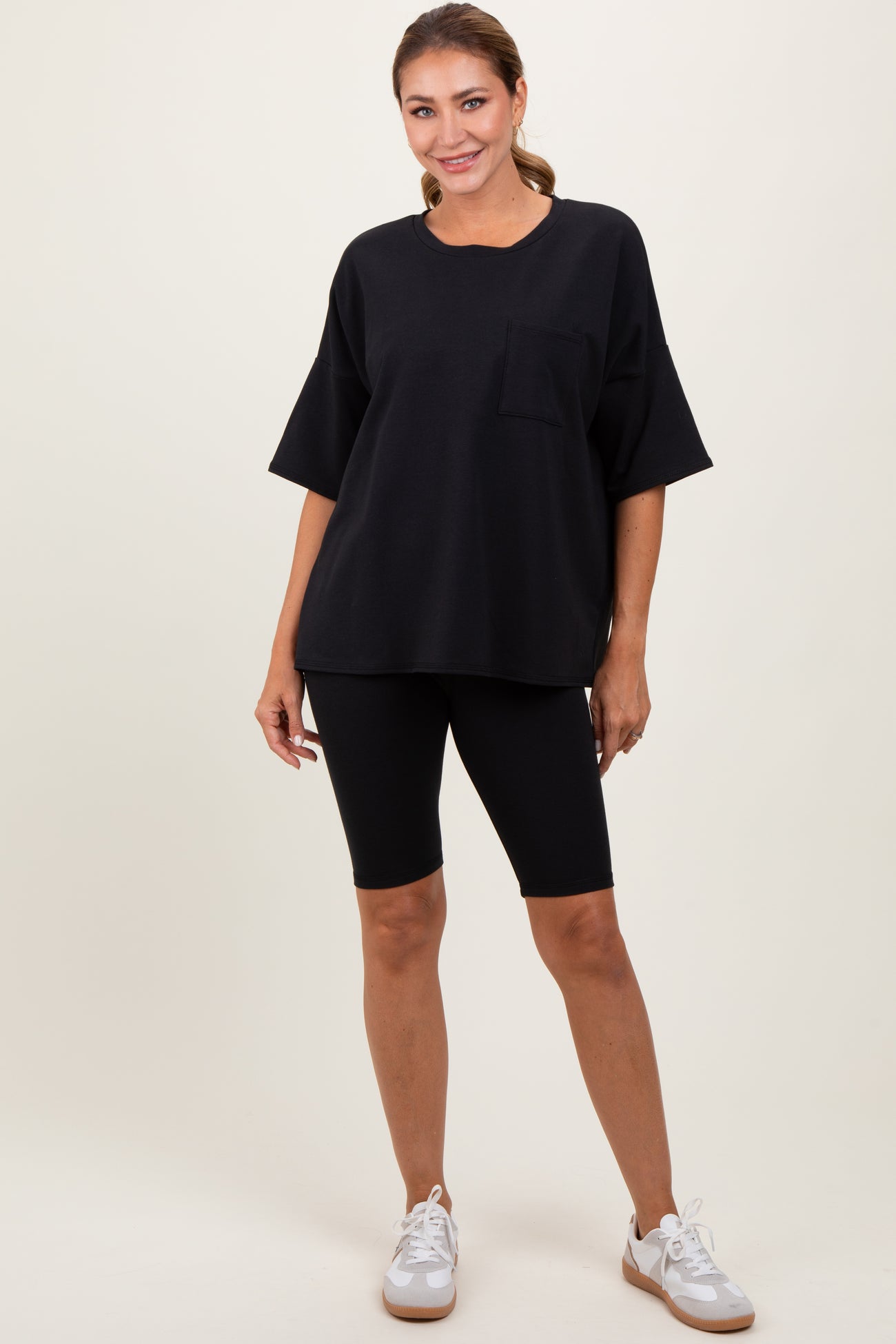 woman wearing a black oversized t-shirt with a pocket and black biker shorts, standing with hands on hips