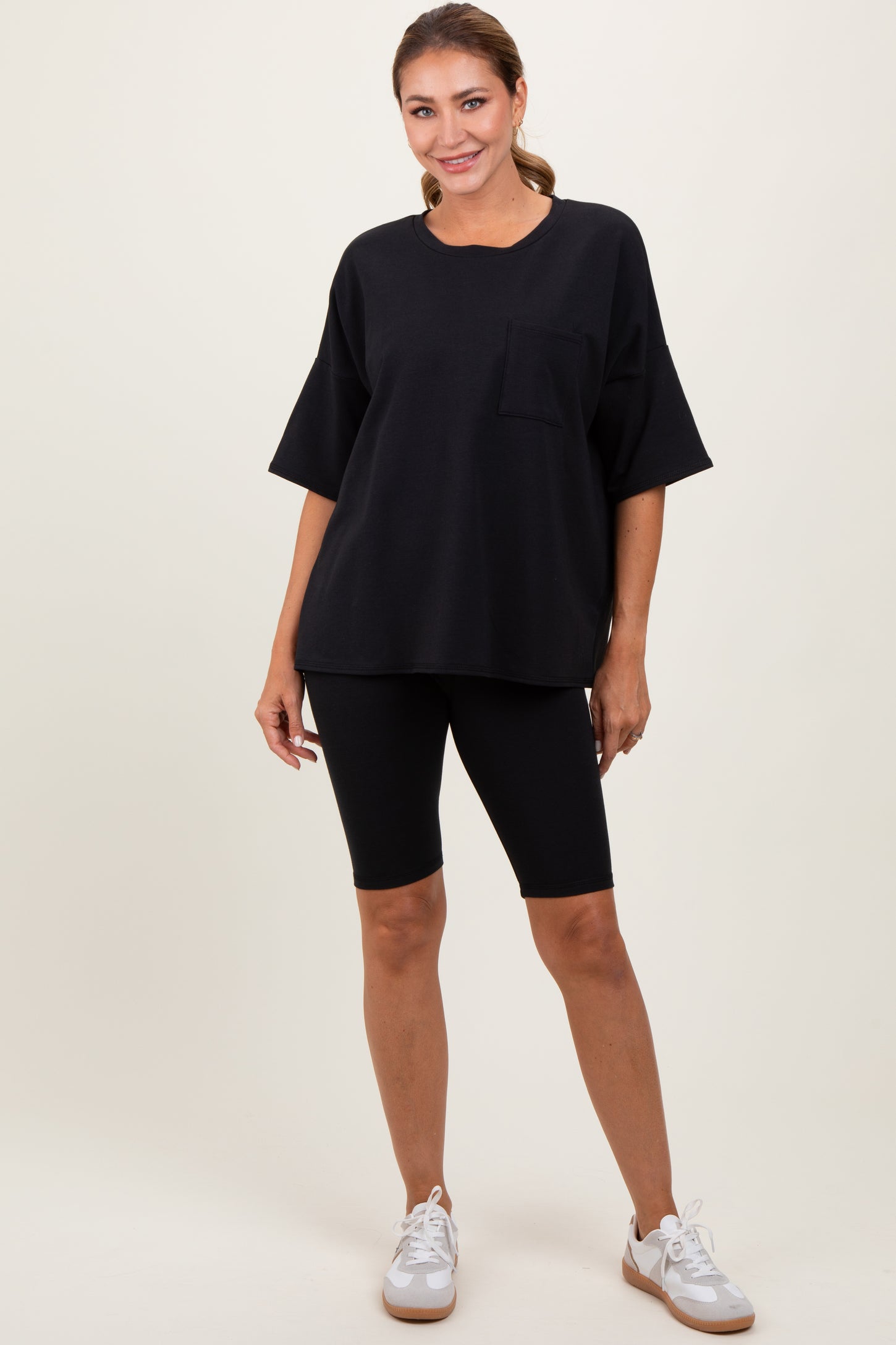 woman wearing a black oversized t-shirt with a pocket and black biker shorts, standing with hands on hips