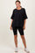 woman wearing a black oversized t-shirt with a pocket and black biker shorts, standing with hands on hips