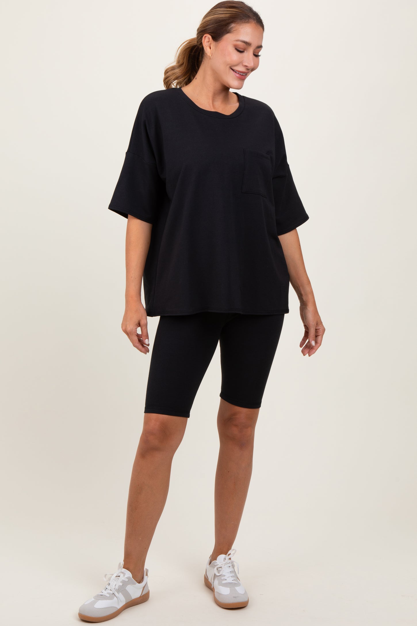 woman wearing a black oversized t-shirt with a pocket and black bike shorts, styled with white sneakers