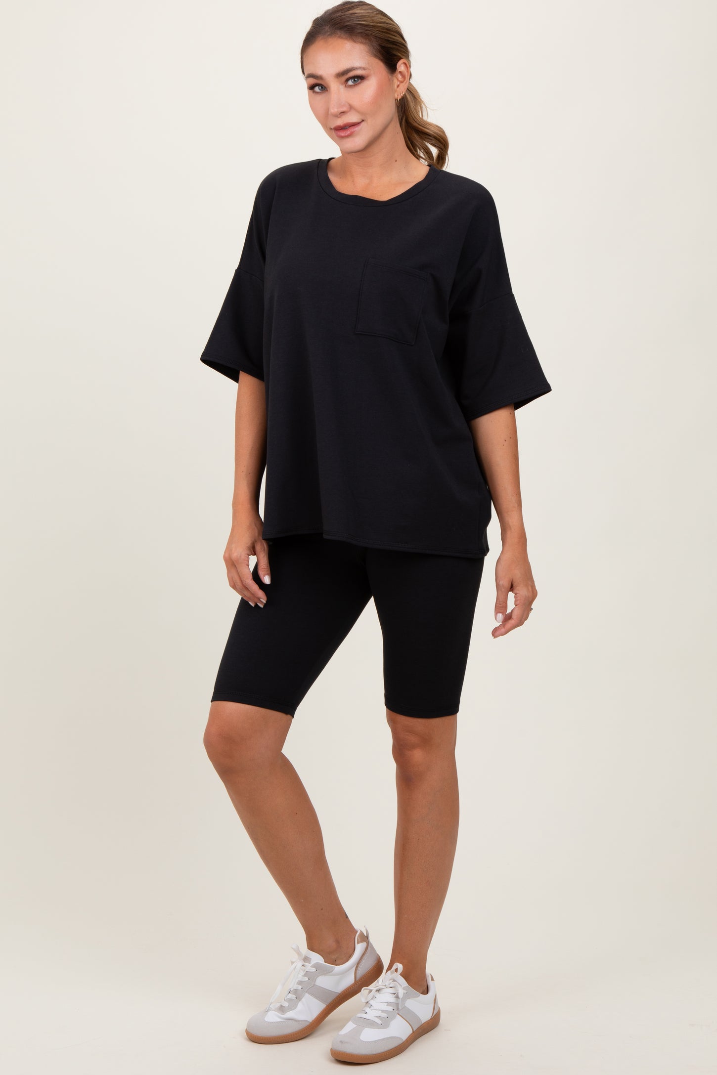 woman wearing a black oversized t-shirt with pocket and black bike shorts, paired with white sneakers