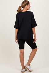woman wearing a black oversized top and black bicycle shorts, standing with her back facing the camera