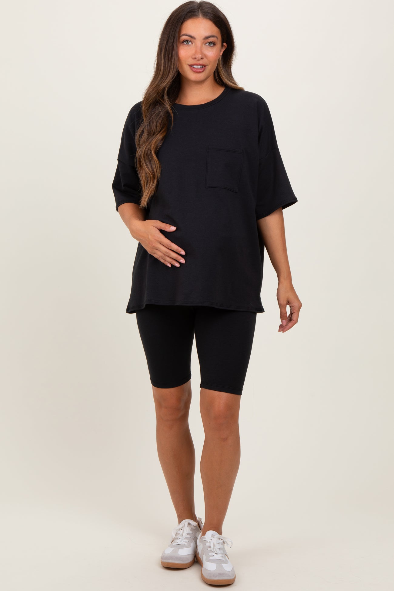 woman wearing a black oversized maternity t-shirt and black biker shorts, holding her baby bump