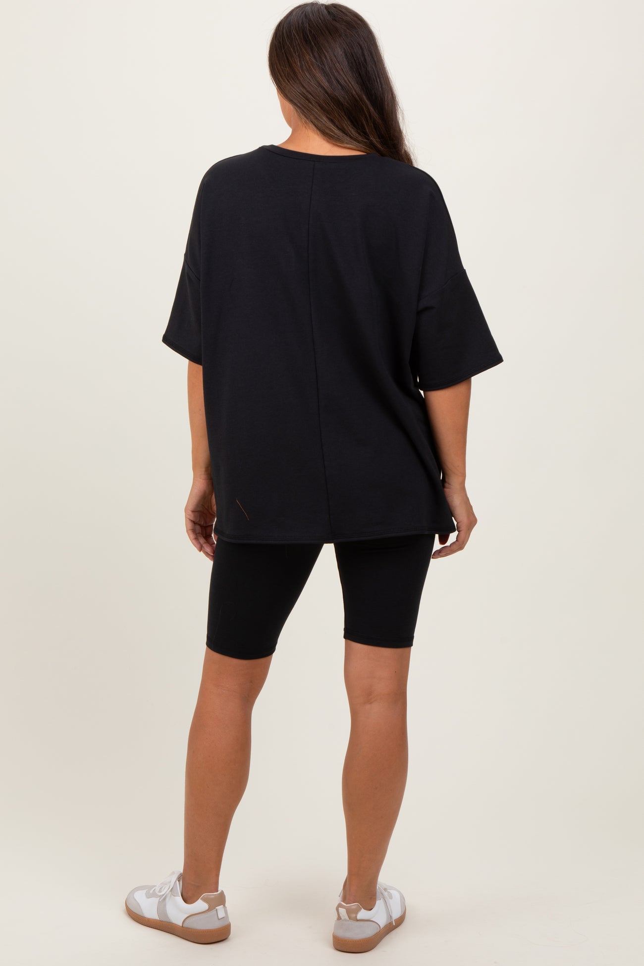 woman wearing a black oversized maternity t-shirt and black bike shorts, standing with her back facing the camera