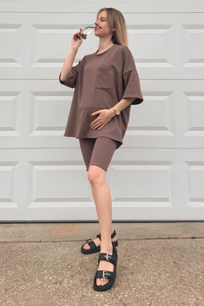 woman wearing a brown maternity oversized t-shirt with a pocket and matching bike shorts, accessorized with sunglasses and sandals
