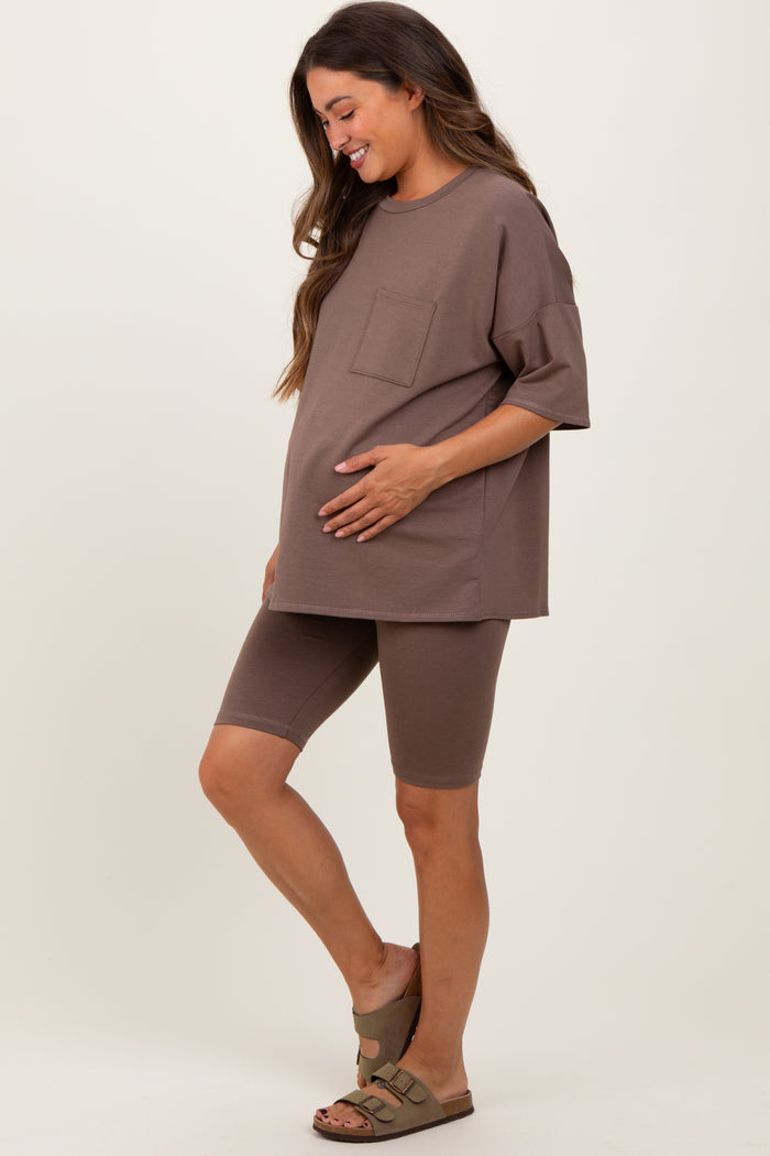 woman wearing a brown maternity oversized t-shirt and matching bike shorts, gently cradling her baby bump