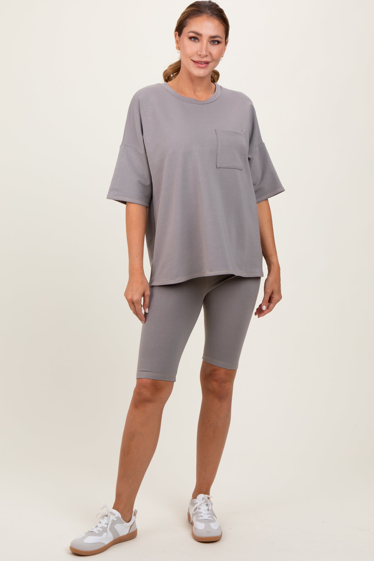woman wearing a gray oversized t-shirt with a pocket and gray bike shorts, posing with one hand on her hip