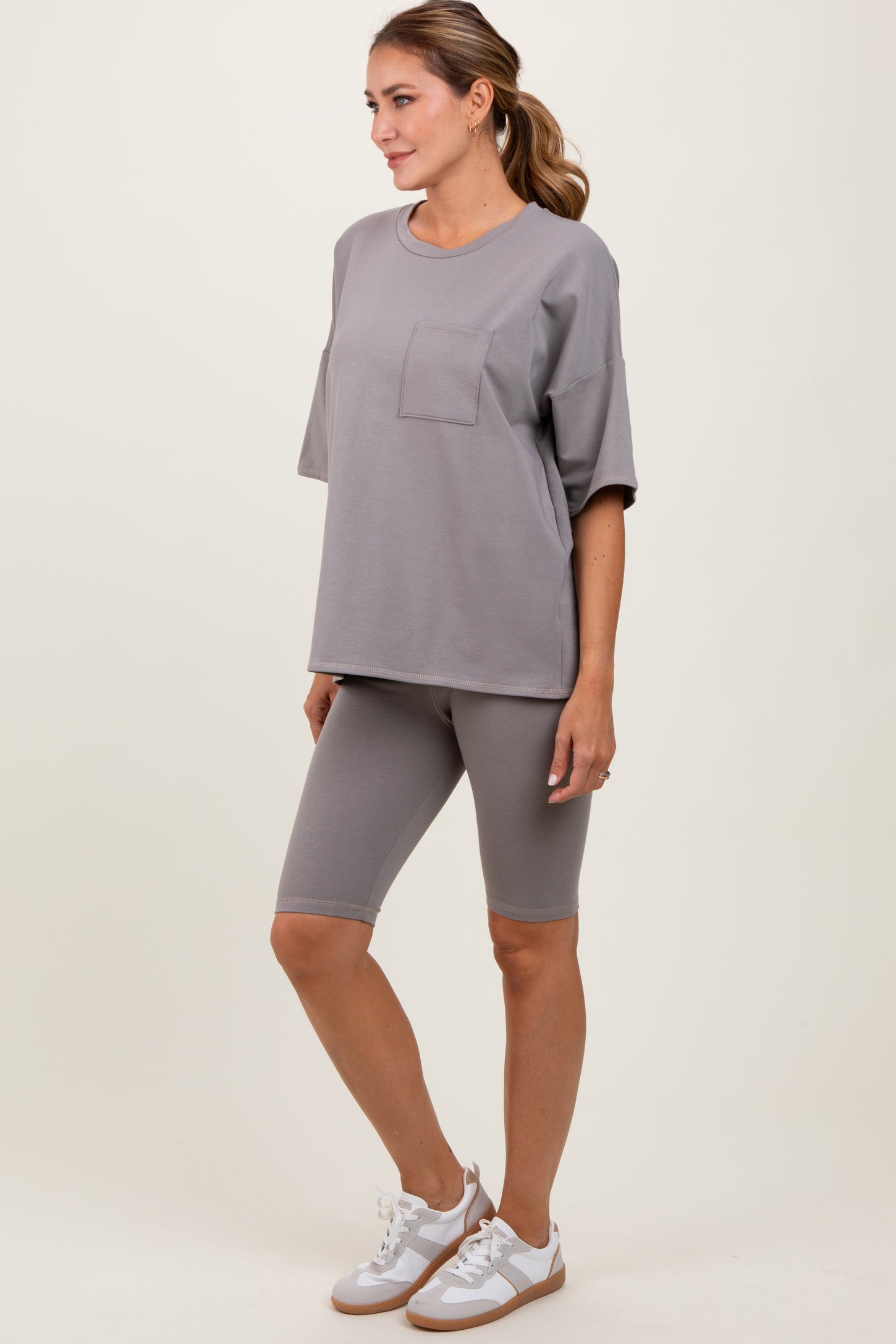 woman wearing a gray oversized t-shirt with pocket and matching gray bike shorts, standing in a relaxed pose