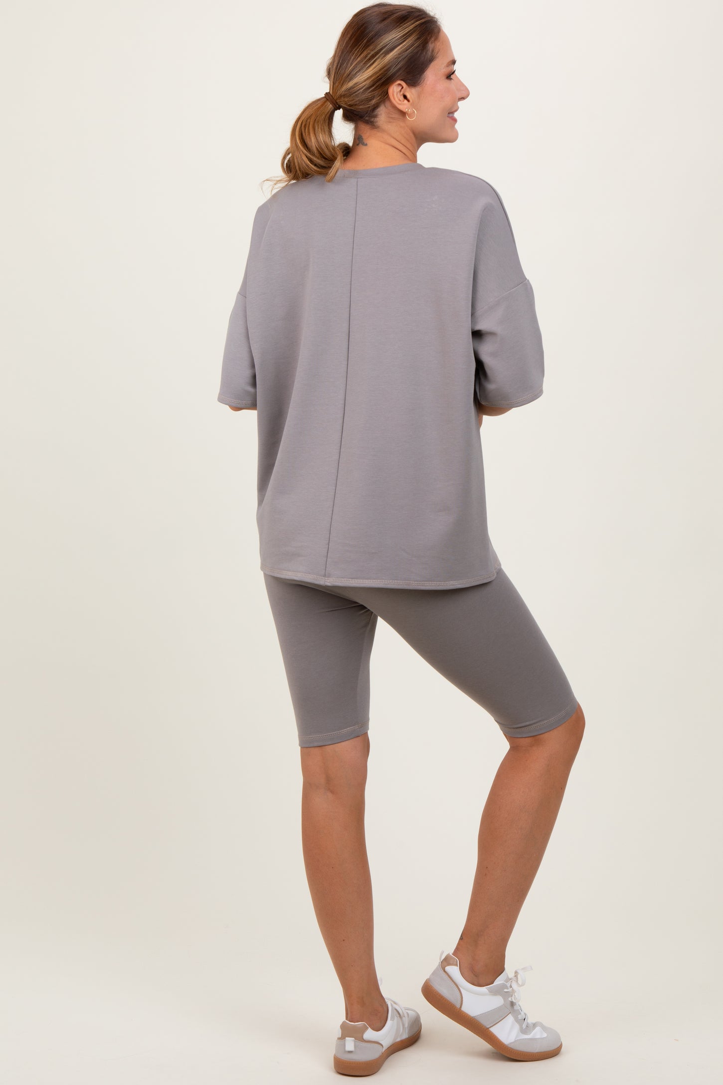 woman wearing a gray oversized sweatshirt and matching bike shorts, standing in a relaxed pose