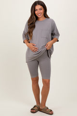 woman wearing a gray oversized maternity top and matching bike shorts, holding her baby bump