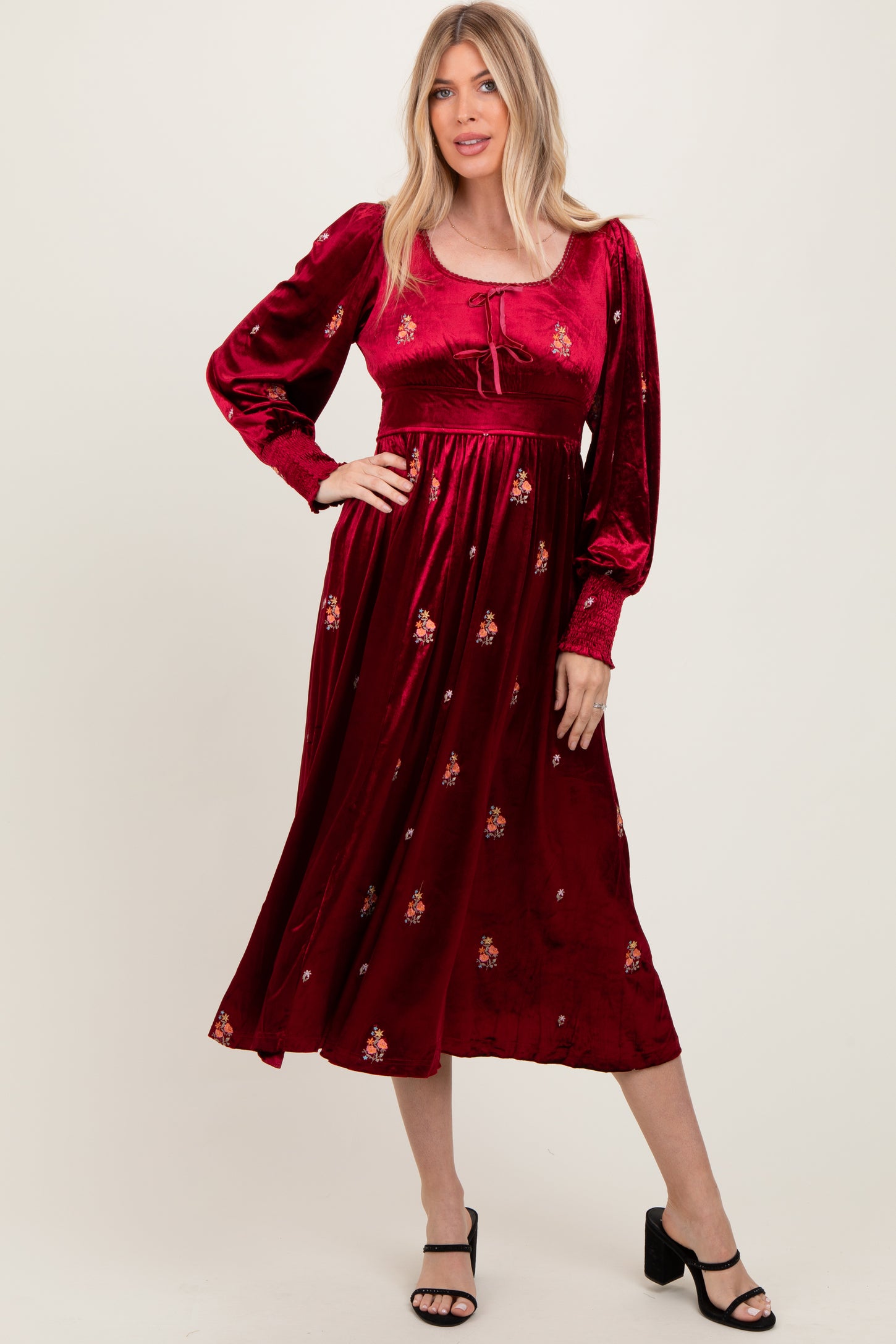 woman wearing a red velvet maxi dress with floral embroidery and long sleeves, paired with black strappy heels