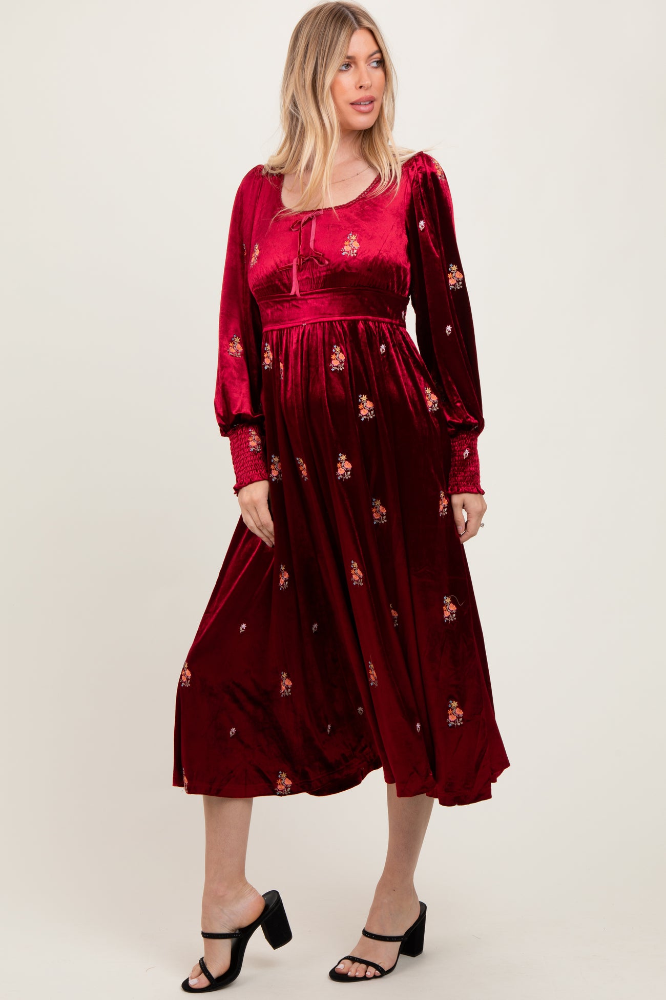 woman wearing a burgundy long sleeve dress with floral embroidery and a flowy skirt, standing in a relaxed pose