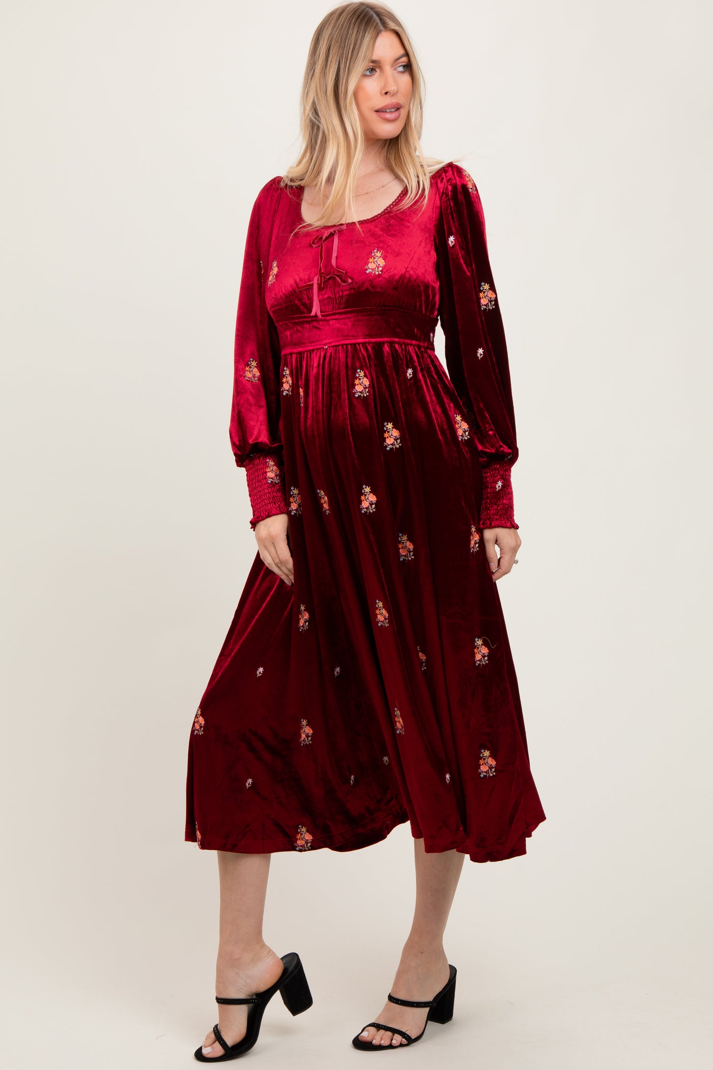 woman wearing a burgundy long sleeve dress with floral embroidery and a flowy skirt, standing in a relaxed pose