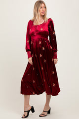 woman wearing a burgundy long sleeve dress with floral embroidery and a flowy skirt, standing in a relaxed pose