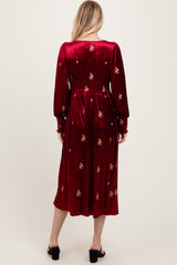 woman wearing a burgundy long sleeve velvet dress with floral embroidery and a cinched waist, view from the back